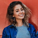 A woman in a denim jacket smiling brightly against a vibrant red and blue background.